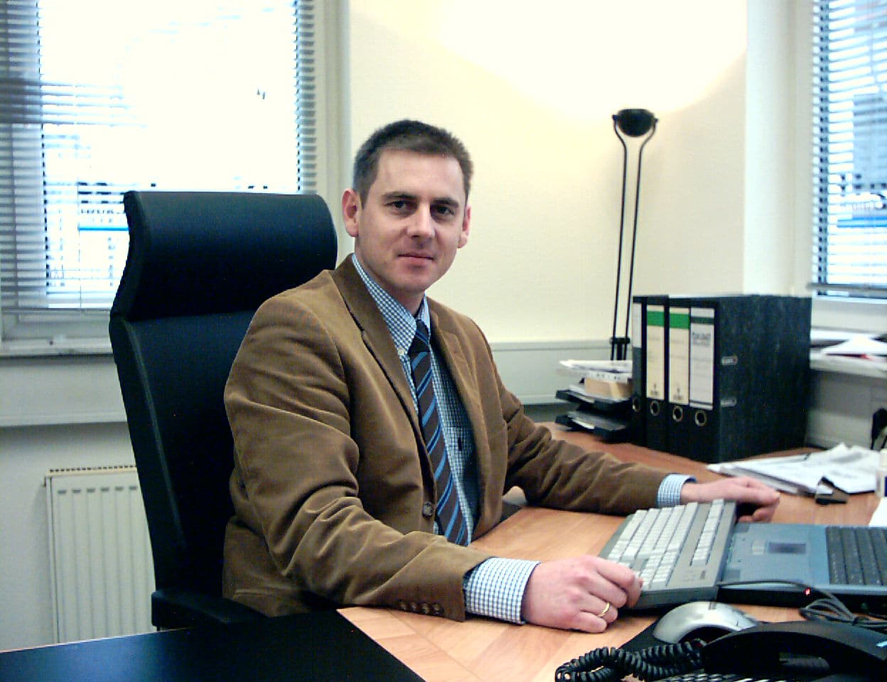Gründer von ProStaff Alexander Fuchs sitzt an seinem Schreibtisch und lächelt in die Kamera